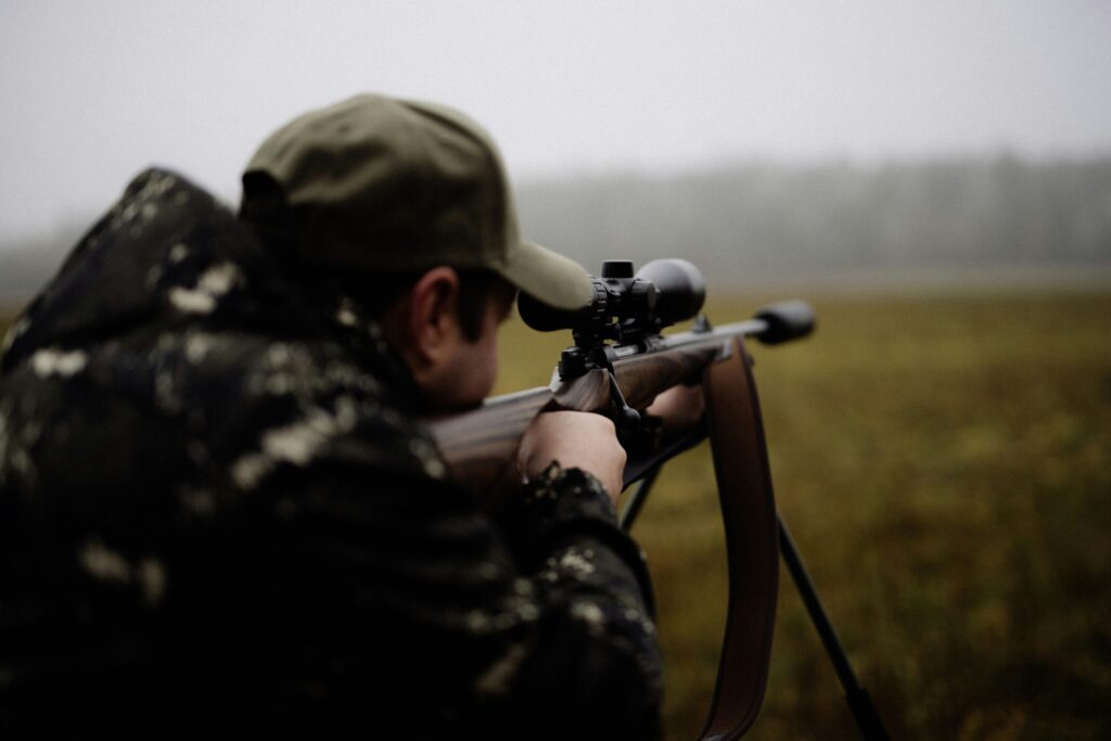 Camouflaged shooter aiming a scoped rifle during professional farm pest control in Wiltshire