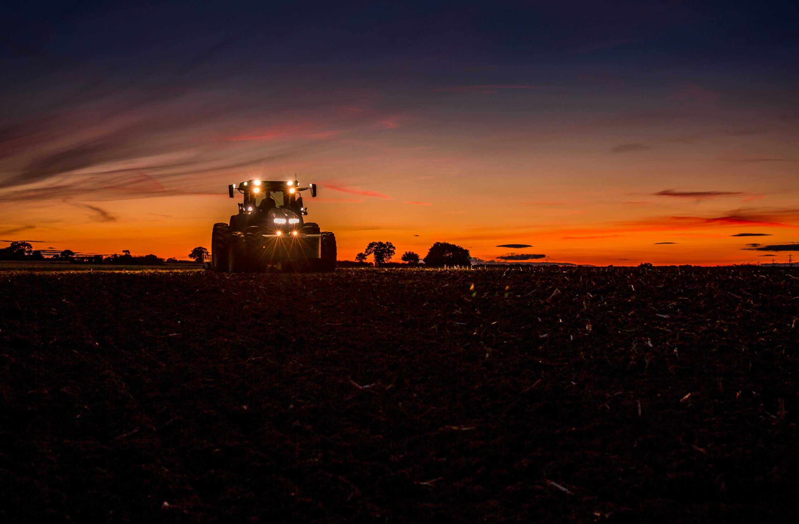 Tractor working a dark arable field at sunset near Swindon for farm pest control and wildlife management